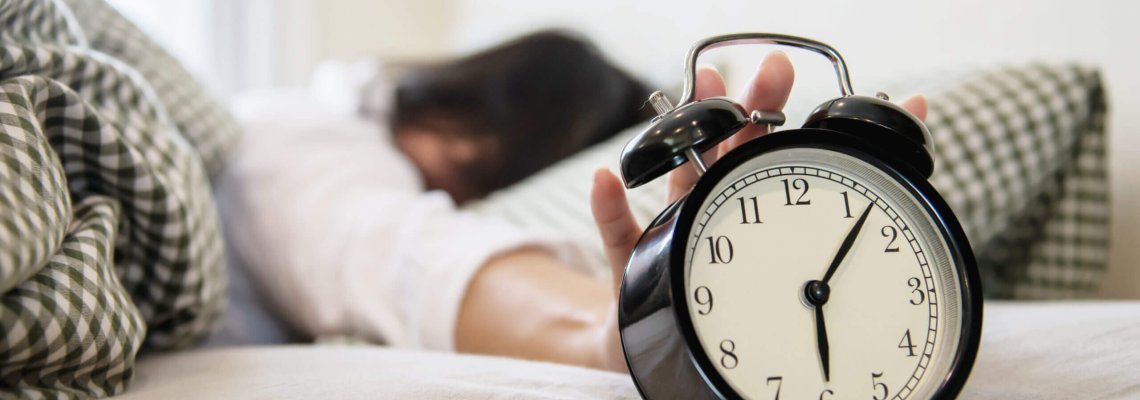 Sleepy woman reaching  holding the alarm clock in the morning with late wake up - every day life at home concept